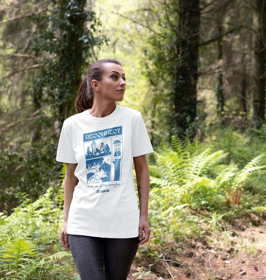 Woman in a forest wearing a white t-shirt. T-shirt features large blue print of Scouts around a campfire, a campsite with tents, a camp lantern and trees. Top text reads 'Reconnect'. Bottom text in cursive reads 'Meet me at the campfire'. Scouter logo sits at the bottom of the design.