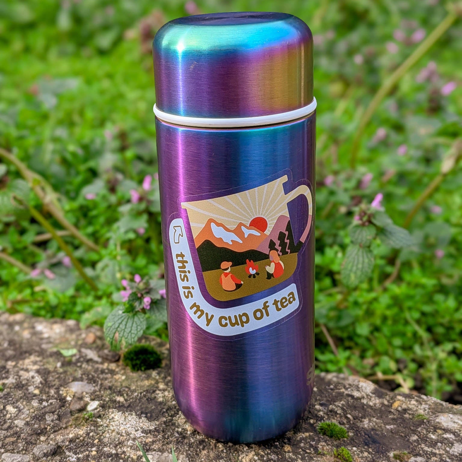 Multicolored thermos with a 'this is my cup of tea' sticker design on a natural background