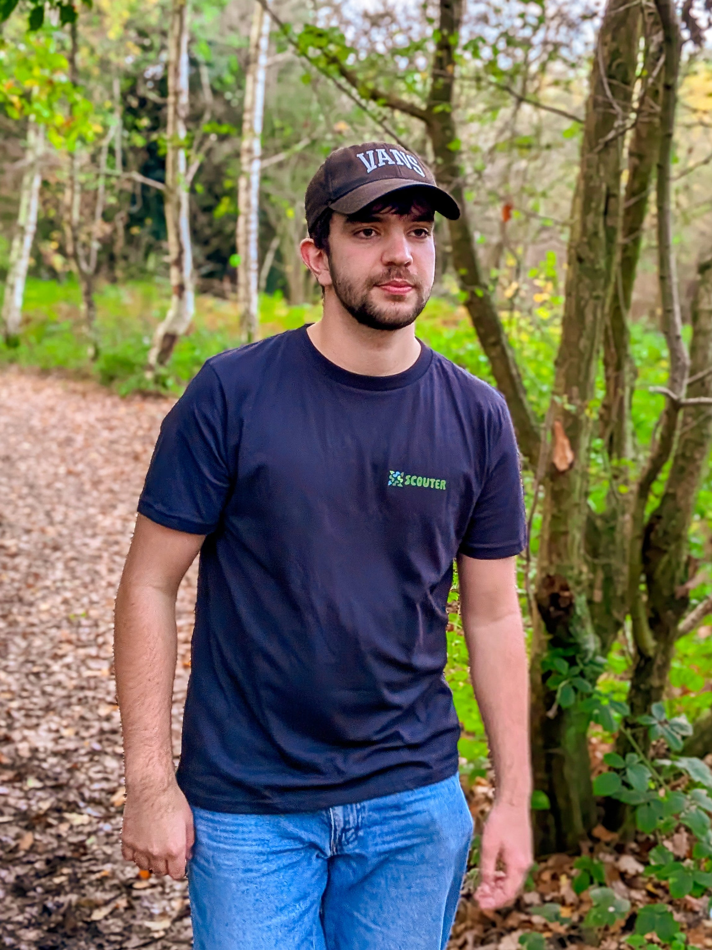 Man wearing a navy blue t-shirt and cap standing on a forest path
