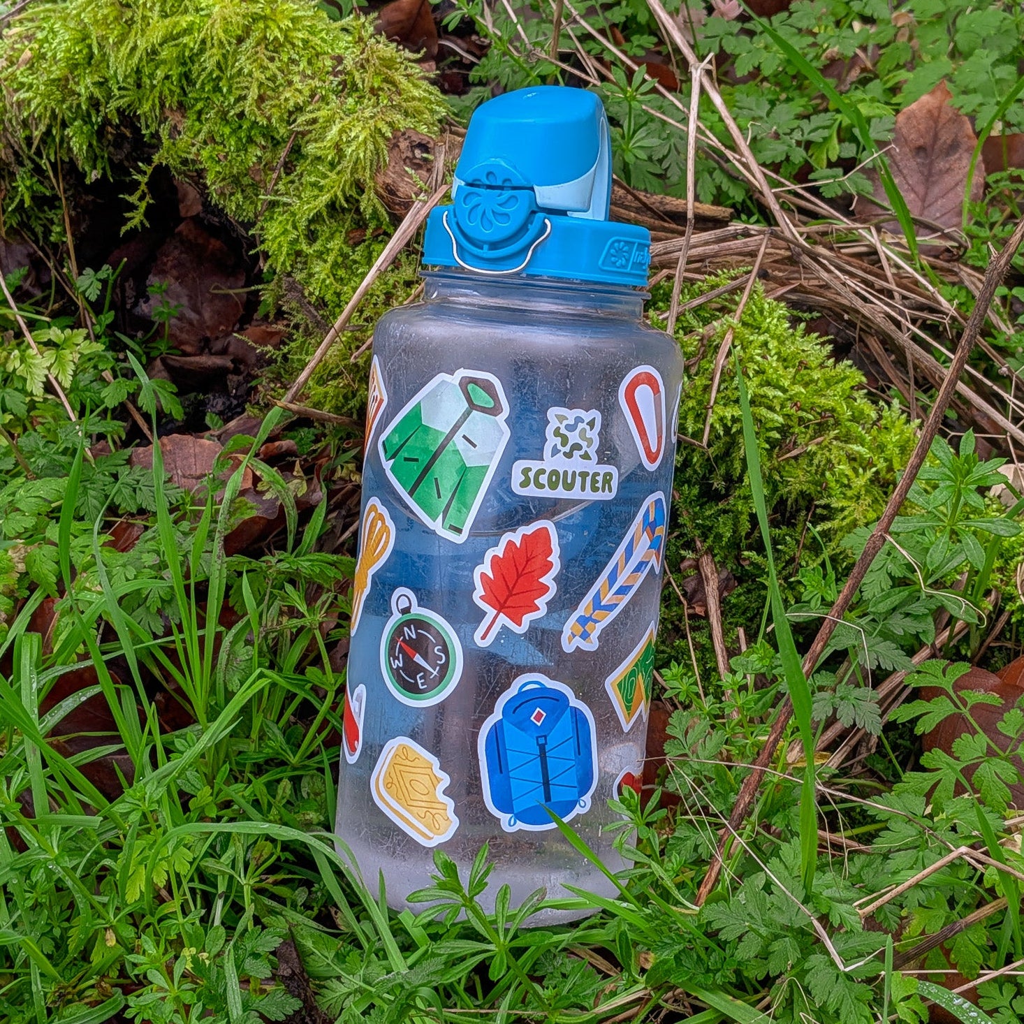 Hiking and Scout themed sticker-covered water bottle in a natural setting with greenery